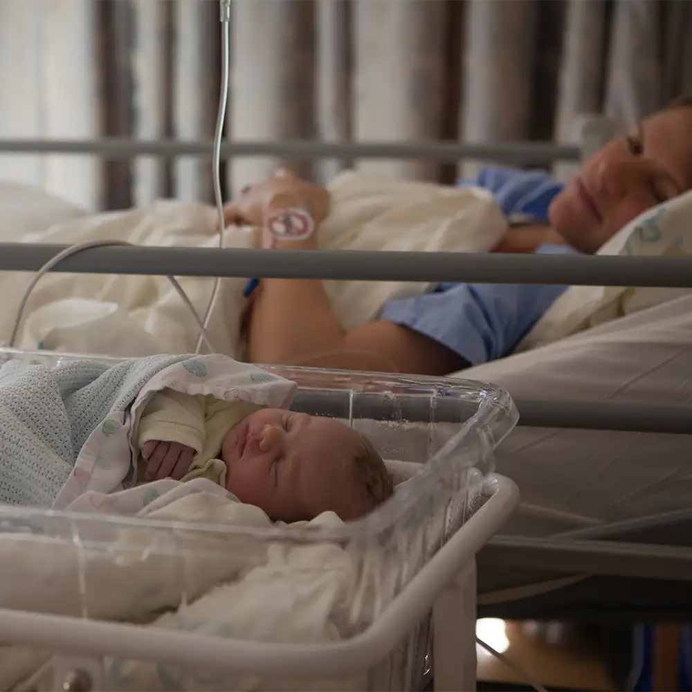 A baby sleeping next to his moms bed in a hospital